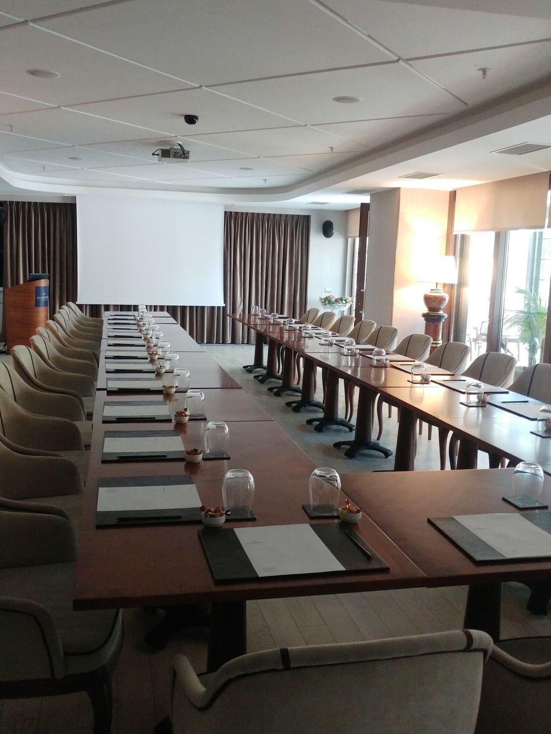 Long table with glasses by plush chairs surrounding a projector screen in Kugu 2 Hall at Warwick Ankara