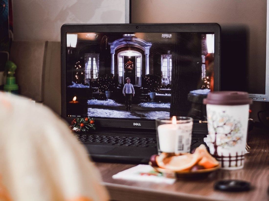 Laptop screen showing a movie spot, set on a desk with a candle and coffee for a cozy night at The Sebel Brisbane
