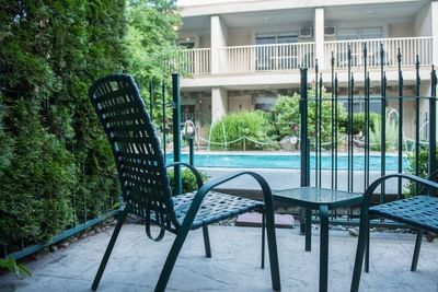 Woven patio chairs near a fence, the swimming pool behind the hedge at Hilltop Inn Salmon Arm