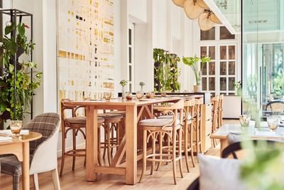 Dining area with wooden furniture, greenery, and an abstract painting on the wall in Opera Restaurant at Park Hyatt Saigon