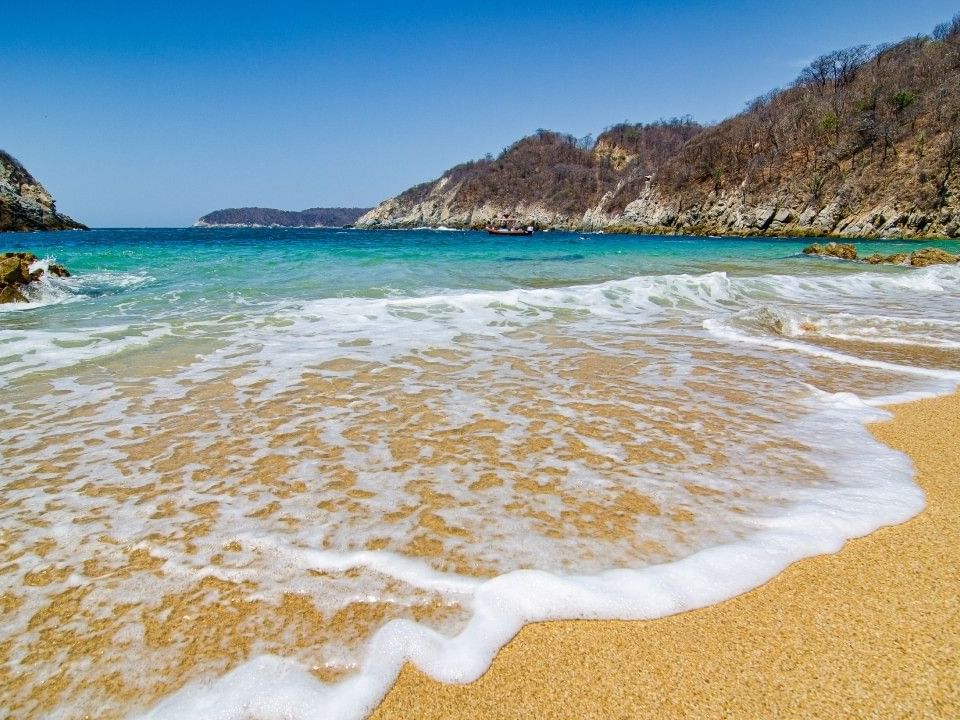 Tropical beach with white waves and clear blue water on a sunny afternoon near Quinta Real Huatulco
