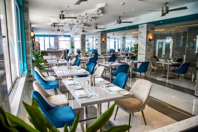 Spacious Remous Bar & Restaurant with blue and grey chairs under ceiling fans at The Abidah Hotel by Accra