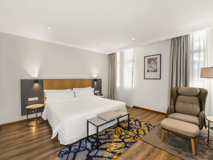 Signature Deluxe King with a bed, art over the headboard, & a cushioned armchair by the window at The Grace Sydney hotel
