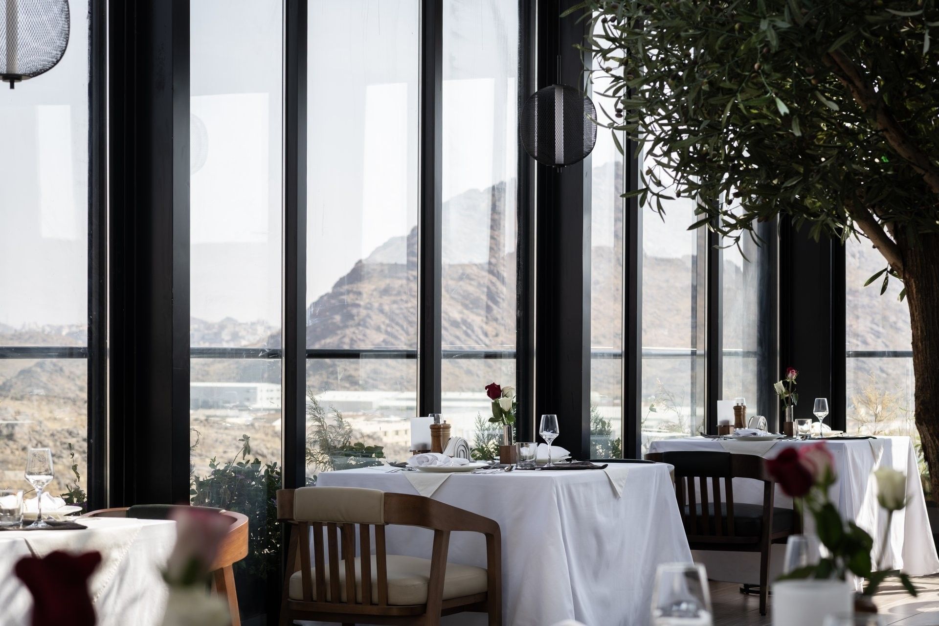 Dining table with wooden chair under a dark pendant light by a window in Karkan Restaurant at Warwick Al Taif Hotel