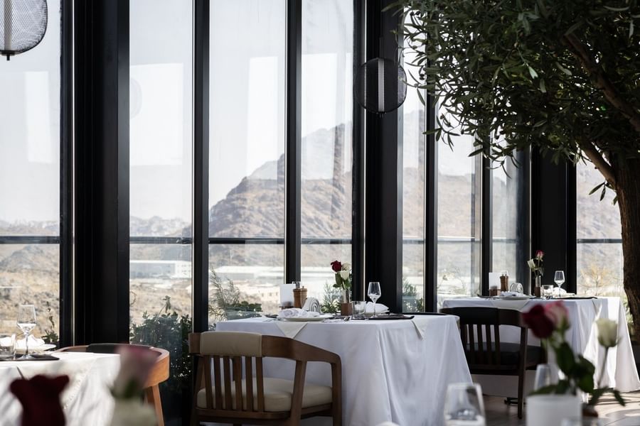 Dining table with wooden chair under a dark pendant light by a window in Karkan Restaurant at Warwick Al Taif Hotel