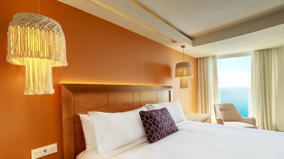 Modern hotel room at Camino Real Veracruz featuring a large bed with a wooden headboard, a bright orange accent wall