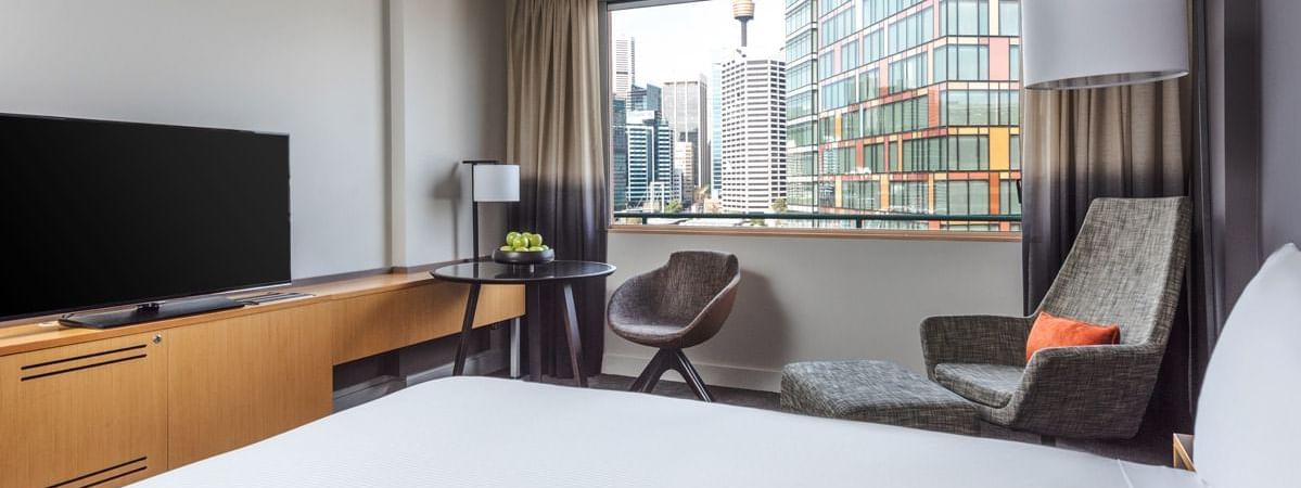 Queen-sized bed with a city skyline view in Deluxe Room at Novotel Sydney on Darling Harbour