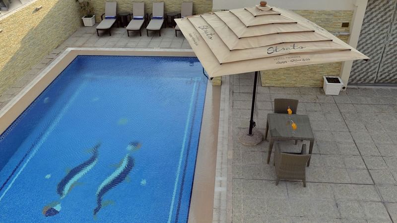 Beverages served on a dining table & sun loungers by the pool in Wellness & Spa at Strato Hotel by Warwick Doha