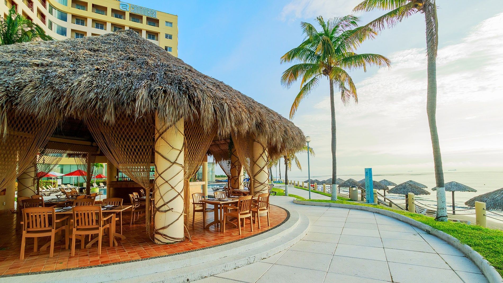 Scenic palapa-style outdoor dining in La Vela overlooking the beach with palm trees and ocean at Camino Real Veracruz