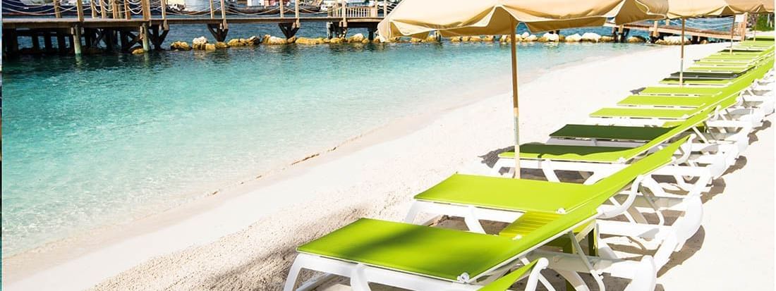 reen loungers by the water under a tan umbrella surrounding a wooden pier near Warwick Paradise Island Bahamas