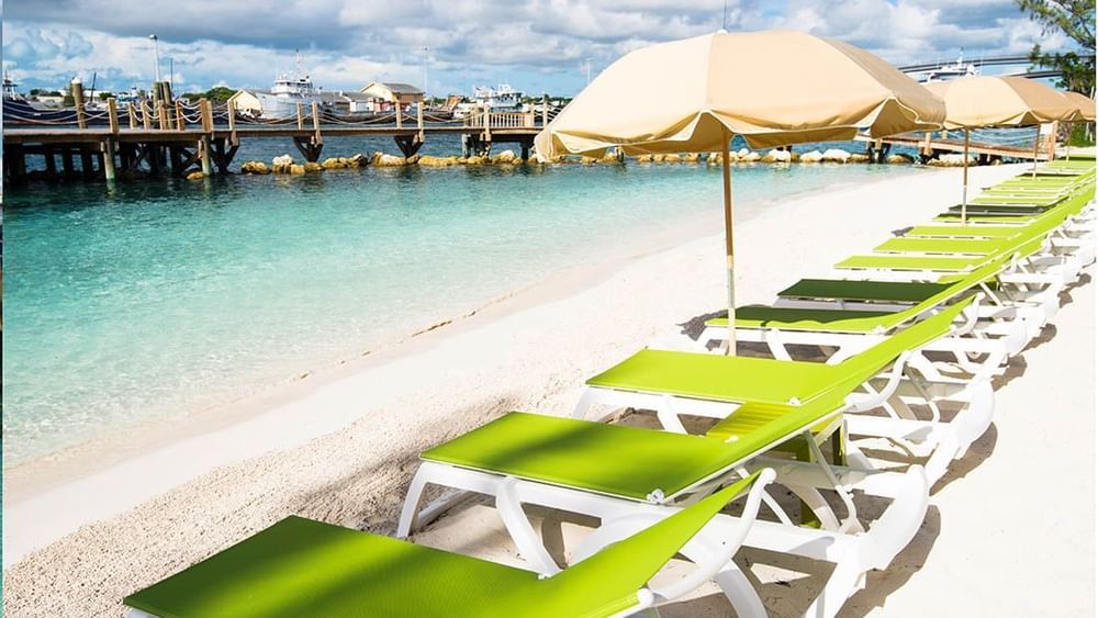 reen loungers by the water under a tan umbrella surrounding a wooden pier near Warwick Paradise Island Bahamas