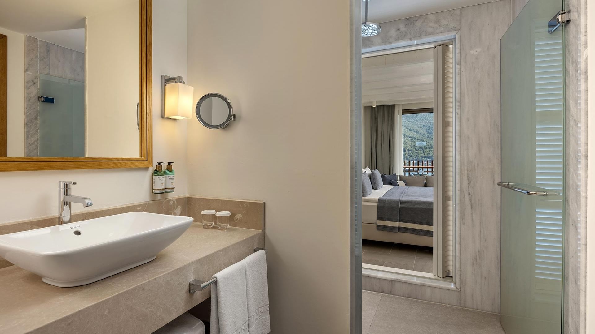 Ванная комната номера с видом на море в отеле Titanic Luxury Collection Bodrum: оснащена стеклянной дверью душевой, выходящей в спальню, просторной раковиной, зеркалом и полотенцами.
