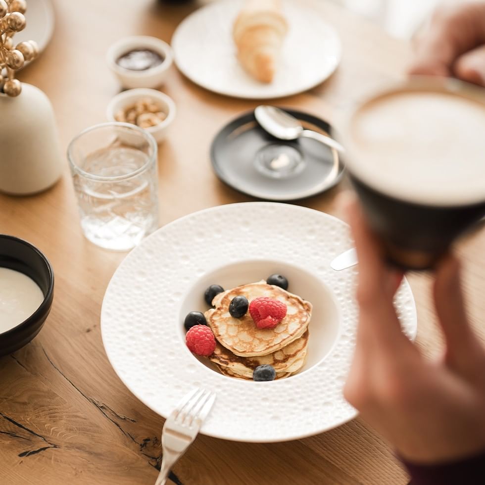 Person genießt Pfannkuchen mit Beeren und Kaffee am Frühstückstisch im day spa.