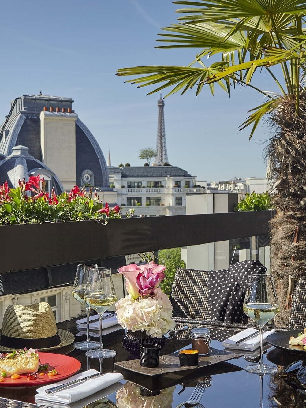 Gourmet plates by wine glasses under a palm tree near the Eiffel Tower view at Warwick Paris Champs Elysées