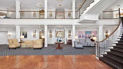 Spacious two-story lobby featuring a grand staircase and sitting areas with armchairs and couches at Avon Old Farms Hotel
