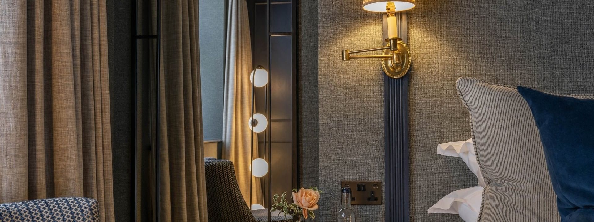 Bedside table with a water glass and flower vase placed by a lamp on the wall at The Capital Hotel, Apartments and Townhouse