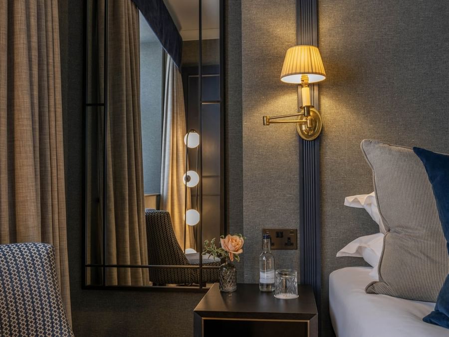 Bedside table with a water glass and flower vase placed by a lamp on the wall at The Capital Hotel, Apartments and Townhouse