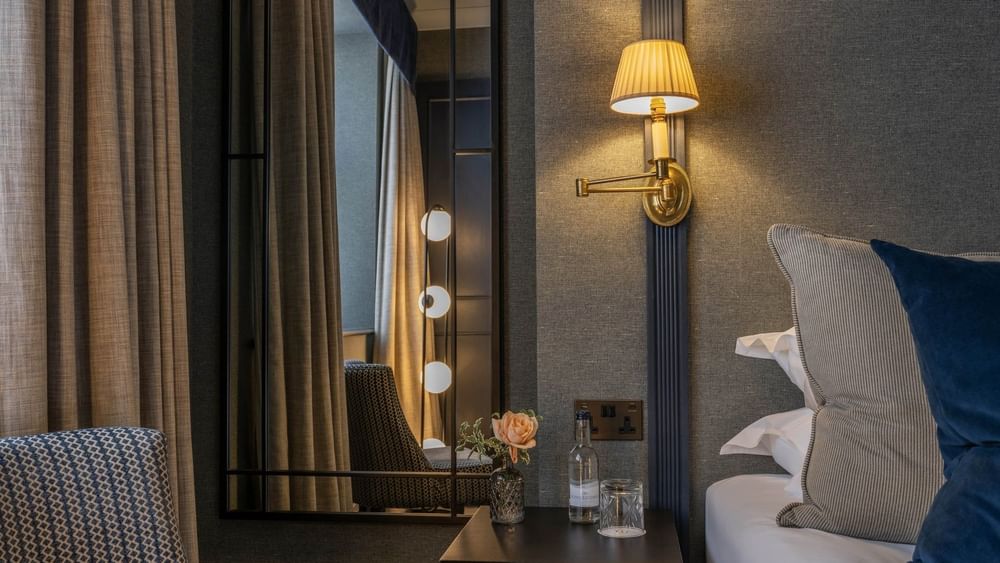 Bedside table with a water glass and flower vase placed by a lamp on the wall at The Capital Hotel, Apartments and Townhouse