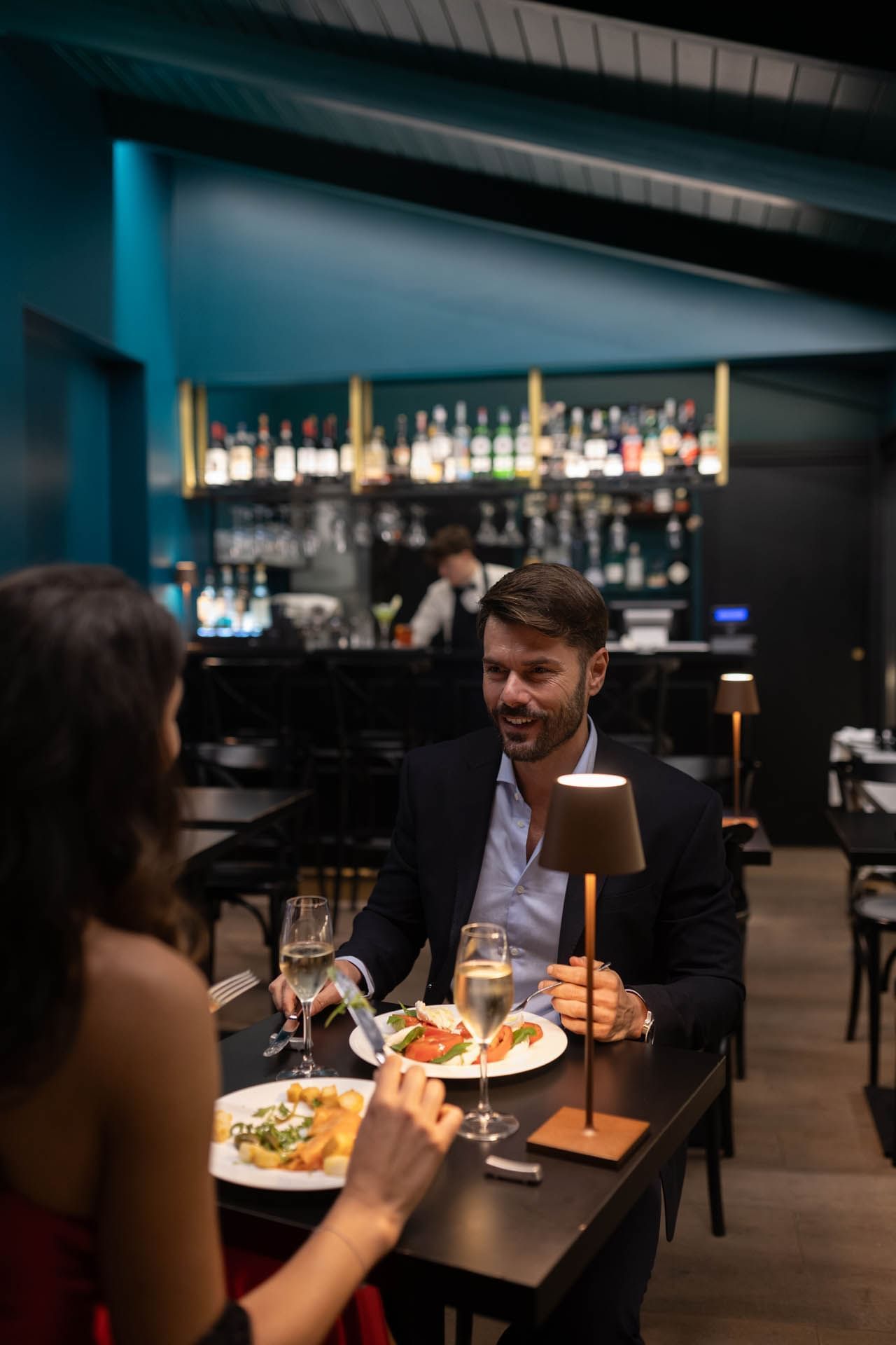A couple enjoys dinner in a stylish restaurant with elegant tables, soft lighting, and a bar at The Guardian Hotel
