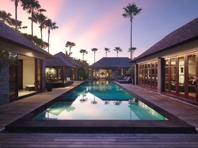 A serene resort pool with tropical architecture and palm trees at sunset, as seen at Peppers Seminyak