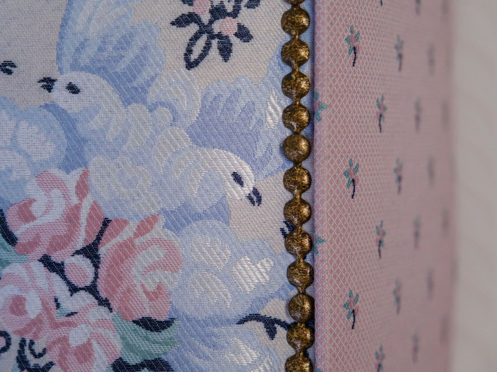 Close-up of floral fabric with blue doves and pink flowers and gold studs on a pink, textured background.