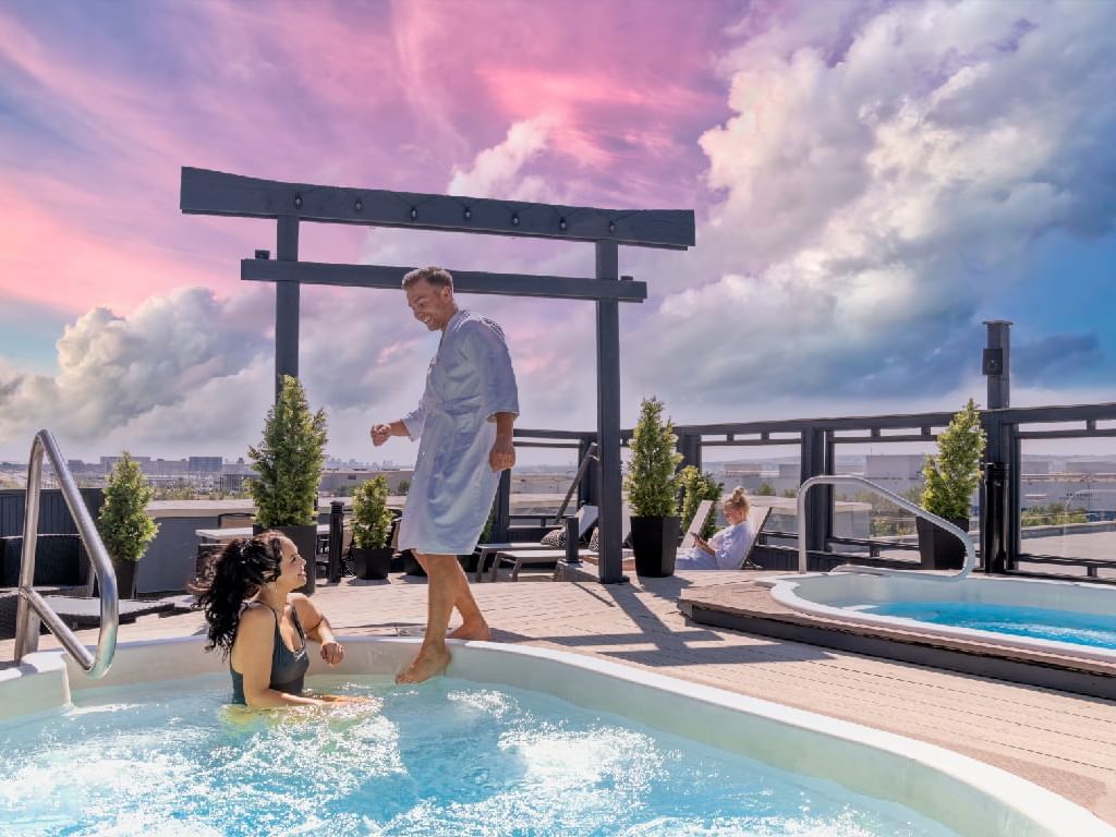 A couple relaxing in a rooftop hot tub with a breathtaking city view at Acclaim Hotel Calgary