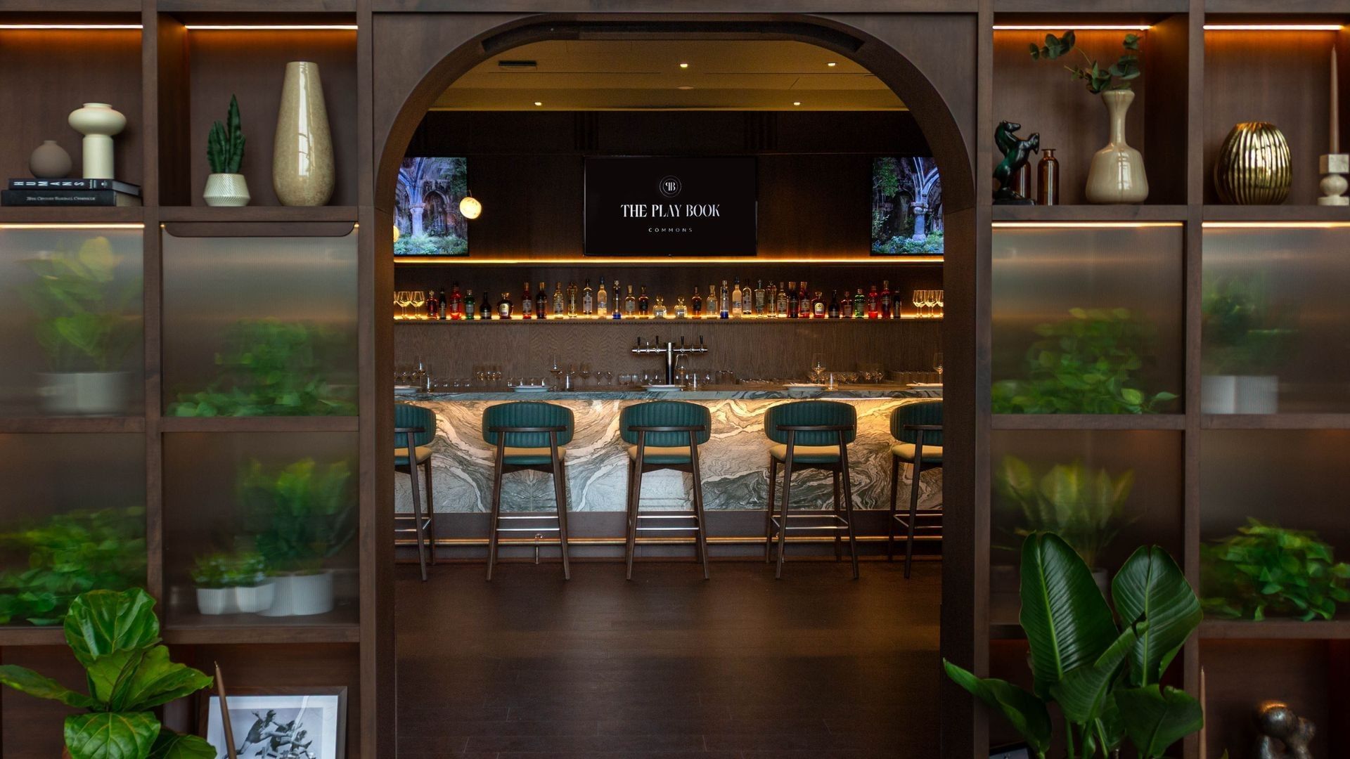 The Play Book Commons bar with green stools by a marbled counter, under a screen at Hotel X Toronto