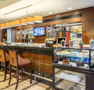 A bar counter with stools and a display case filled with desserts and snacks in Titanic Coffee at Titanic Port Bakırköy