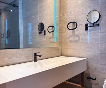 Modern white sink vanity with black fixture under backlit mirror in marble-tiled bathroom at Hotel B3 Sibelius