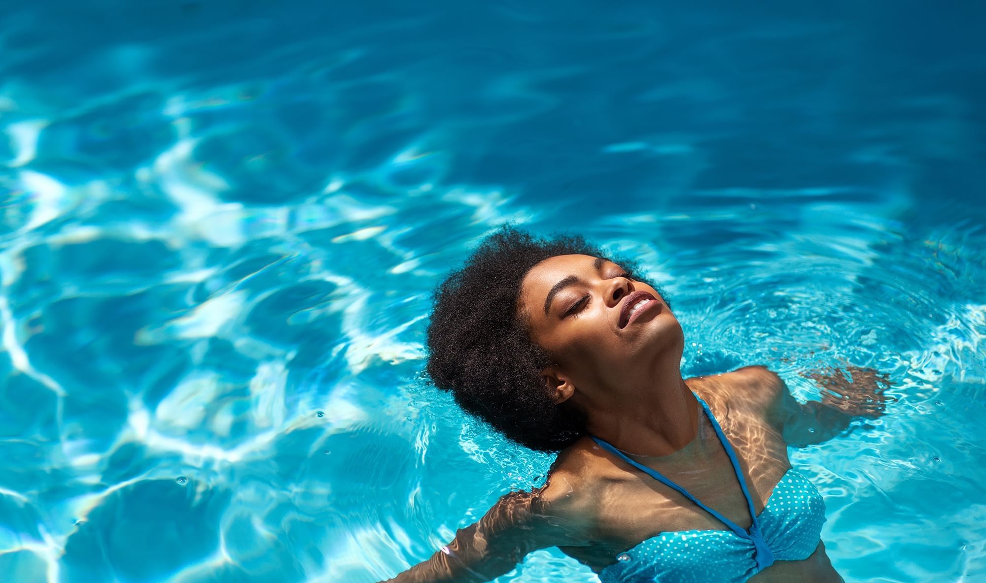 A young lady floating in the pool at Warwick Melrose Dallas