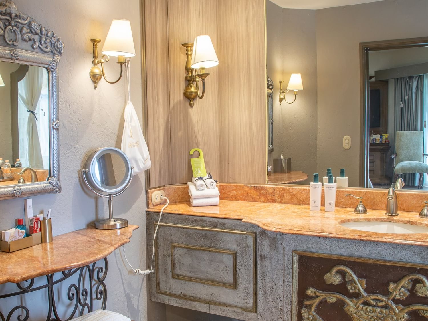 Baño elegante con tocador de mármol, espejo ornamentado y apliques dorados en Quinta Real Guadalajara