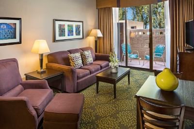Living room with purple sofas, lamps, and patio access with blue chairs at London Bridge Resort