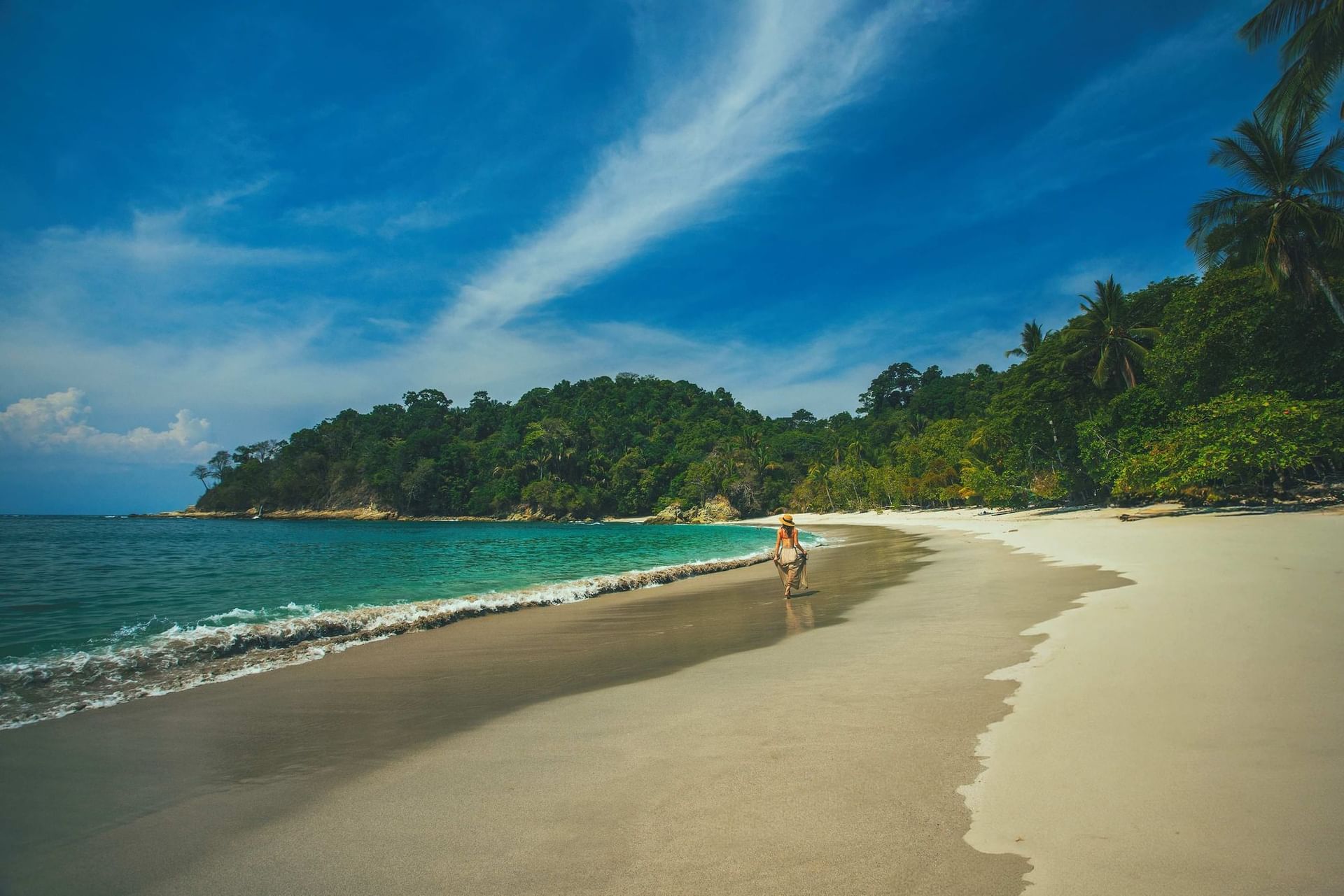 Solitary guest walking on sandy shore beside gentle ocean waves along tropical forest line at Los Altos Resort