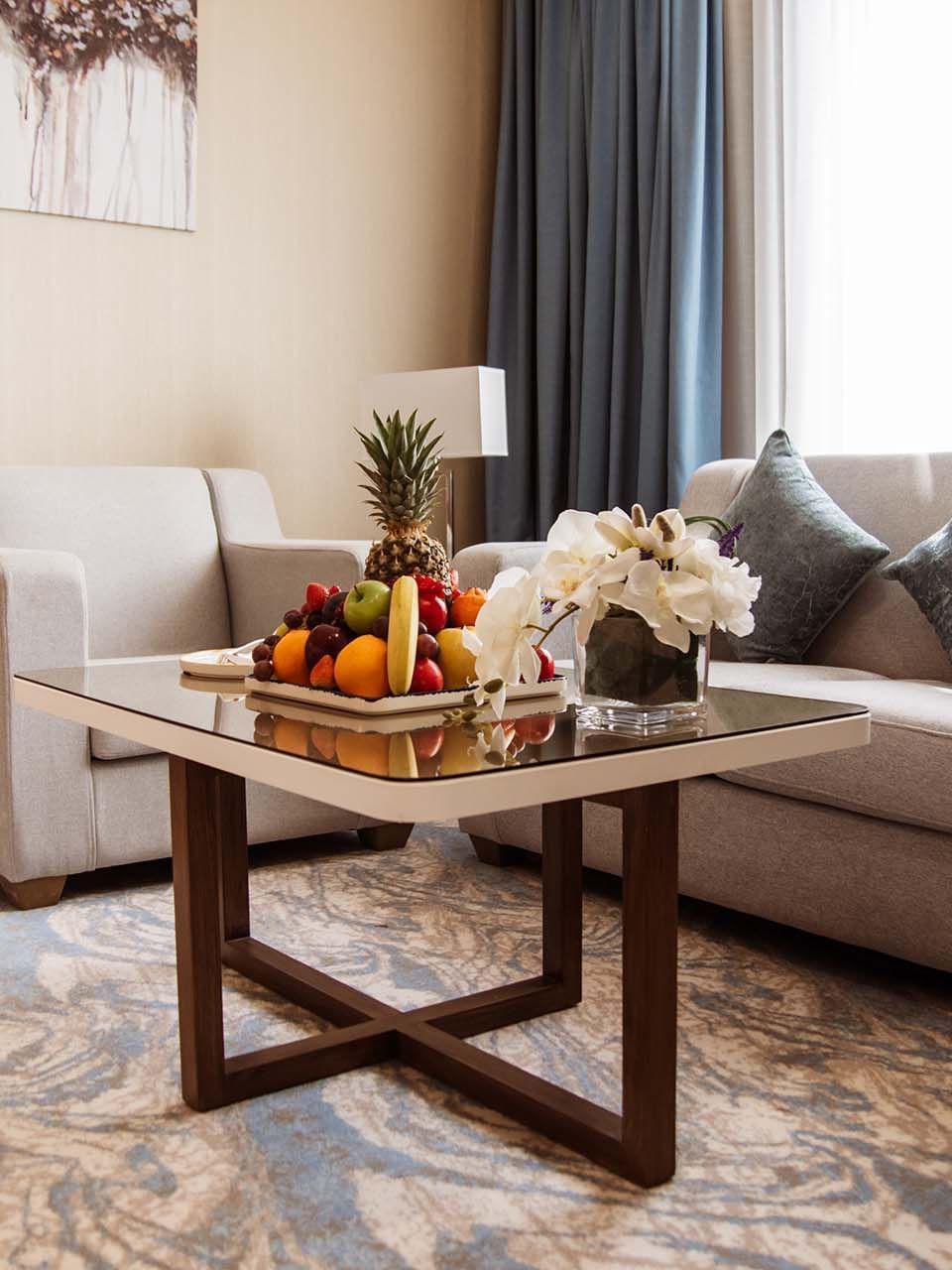 Deluxe Room features Fruit tray on a glass table by a grey sofa and armchair at Cantonal Hotel by Warwick Riyadh