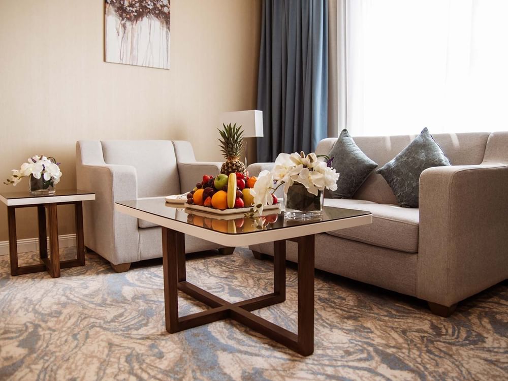 Deluxe Room features Fruit tray on a glass table by a grey sofa and armchair at Cantonal Hotel by Warwick Riyadh