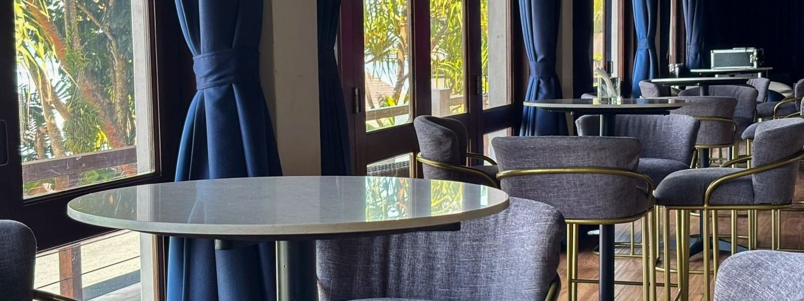 Grey stools by high tables under woven pendant lights near blue curtains in Hibiscus Lounge at Warwick Fiji Resort and Spa