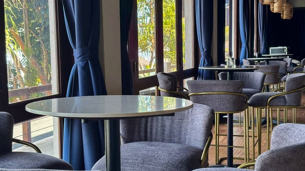 Grey stools by high tables under woven pendant lights near blue curtains in Hibiscus Lounge at Warwick Fiji Resort and Spa