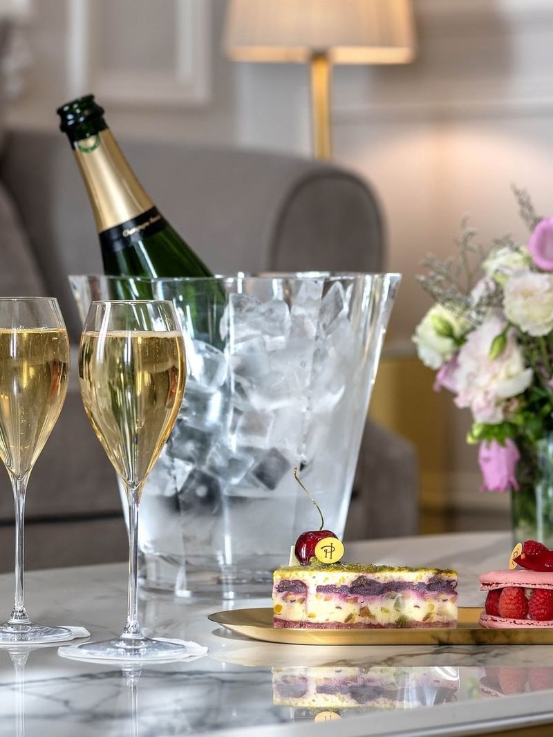 Champagne glasses by a bucket of ice & sweet treats on a table in Prestige Suite – Rue de la Paix Vie at Hôtel Westminster