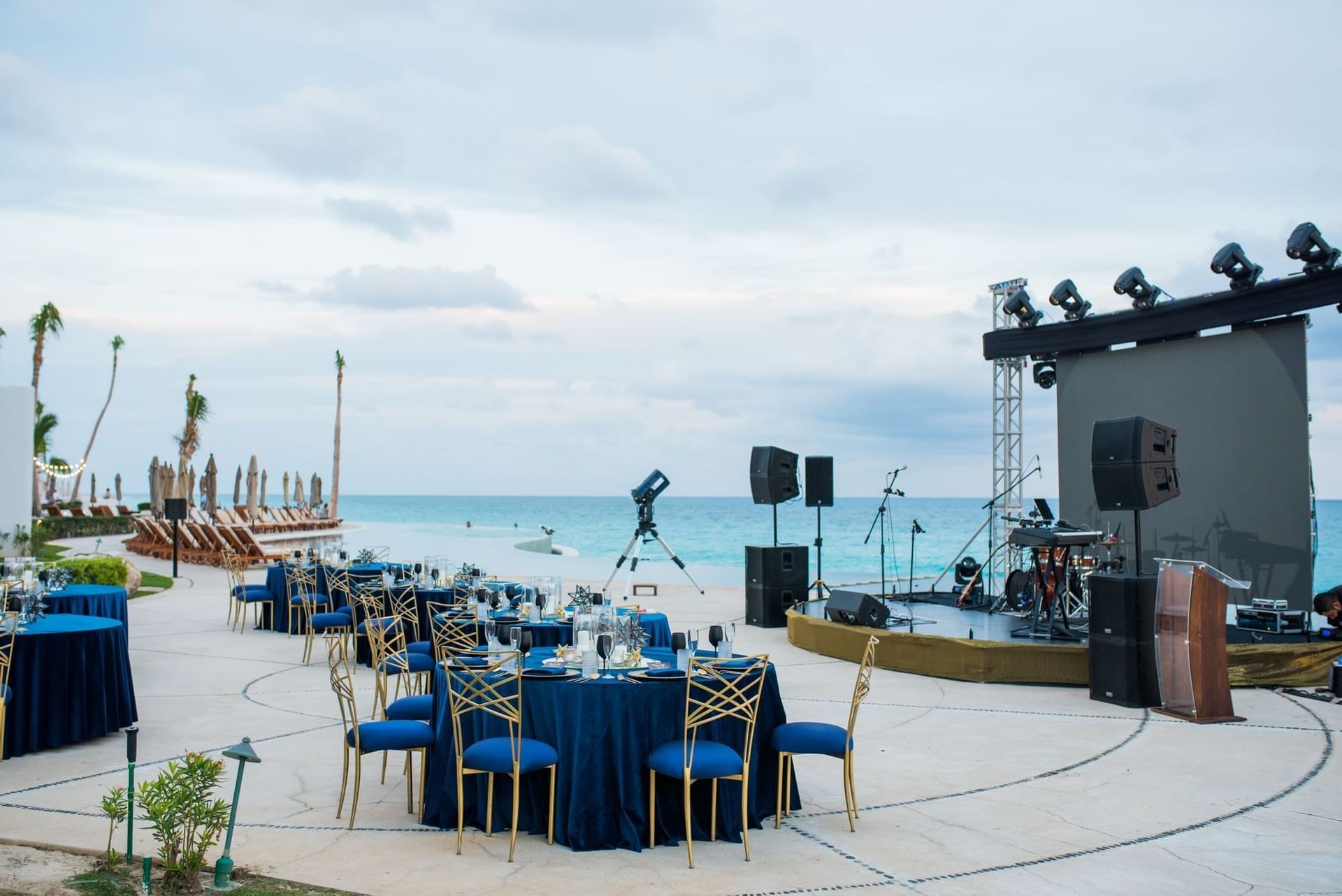 Outdoor event setup with blue tables, chairs, and a stage near the ocean at Marquis Los Cabos Resort