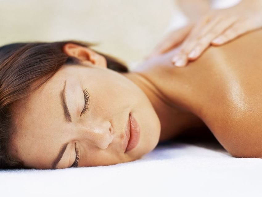 Woman lying down with eyes closed while receiving a back massage from a masseuse.
