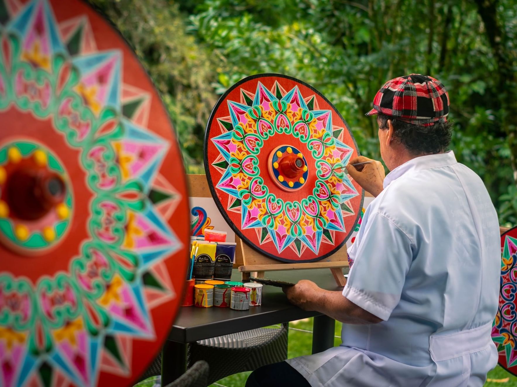 Person painting traditional circular patterns on a cartwheel in an outdoor setting at El Silencio Lodge and Spa