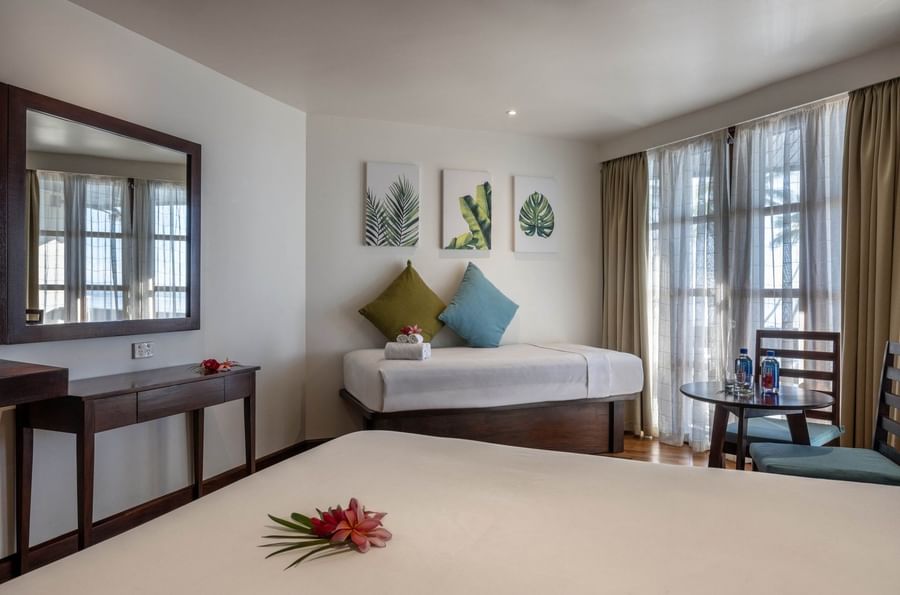 Cozy bed by a wood desk under leaf art with a side table in Ocean View Rooms at Warwick Fiji Resort and Spa