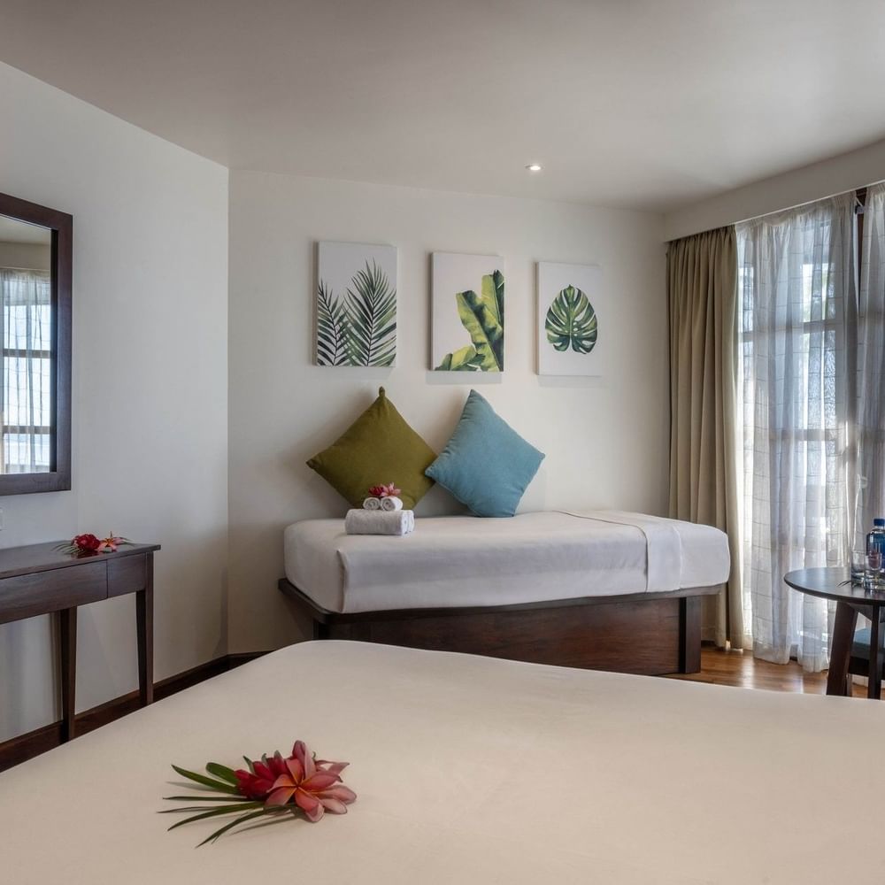 Cozy bed by a wood desk under leaf art with a side table in Ocean View Rooms at Warwick Fiji Resort and Spa