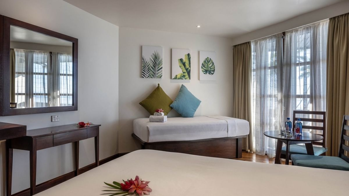 Cozy bed by a wood desk under leaf art with a side table in Ocean View Rooms at Warwick Fiji Resort and Spa