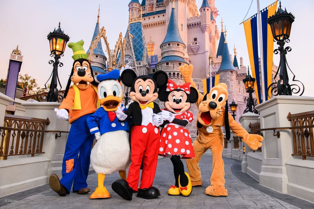 Mickey Mouse, Donald Duck, Goofy, and Pluto mascots standing in front of Cinderella Castle near The Grove Resort & Water Park