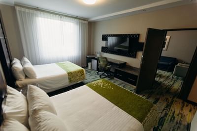 Two comfortable queen beds with green runners by a desk under a wall-mounted TV in Suite at Hotel Mirra
