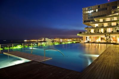 Luxurious outdoor infinity pool with illuminated city skyline view at Hotel Cascais Miragem Health & Spa