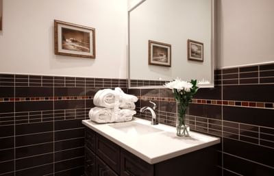 A modern, clean bathroom with brown tiles, floral accents, dark cabinetry, hotel robes, and a sleek light-up mirror.