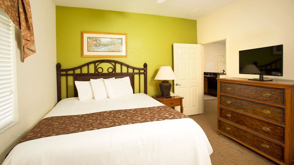 A wide view of a hotel room with a king-sized bed, dresser, and TV