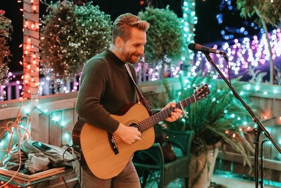 Male musician playing acoustic guitar & singing into microphone at Cambria Pines Lodge, one of the top hotels in Cambria, CA
